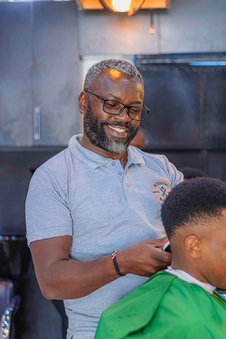 A barber smiling while trimming a client's neckline